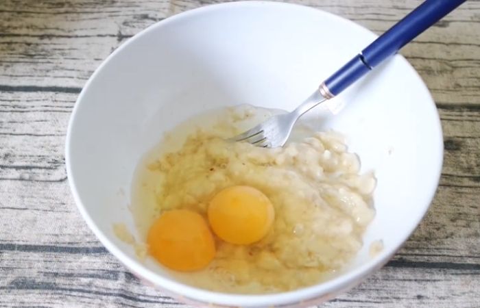 Đập trứng vào bát chuối để tạo thành hỗn hợp pha bột bánh pancake yến mạch